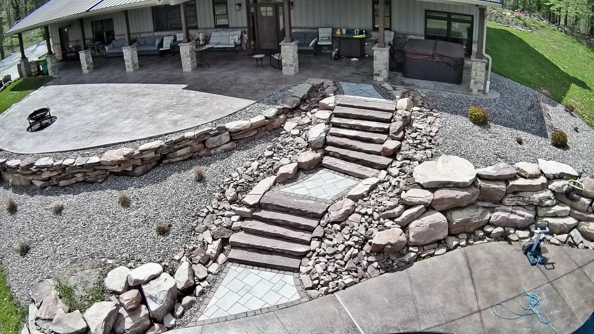 Terraced stone walls and broad steps connecting a paver walkway to a covered patio